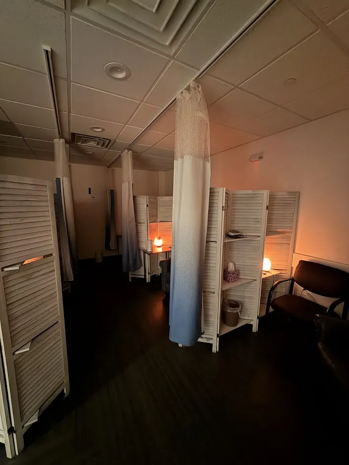 Our Bridgewater treatment room in low light, each treatment space set apart by wooden screens and a curtain, with a salt lamp glowing in each.
