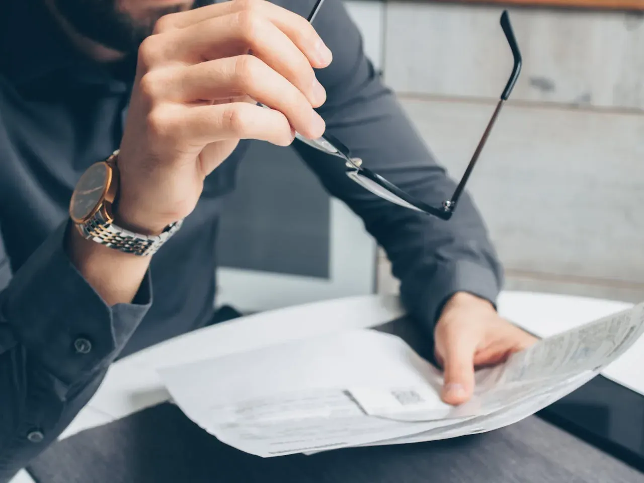 A man's hands holding a pair of glasses while turning the pages of printed notes.