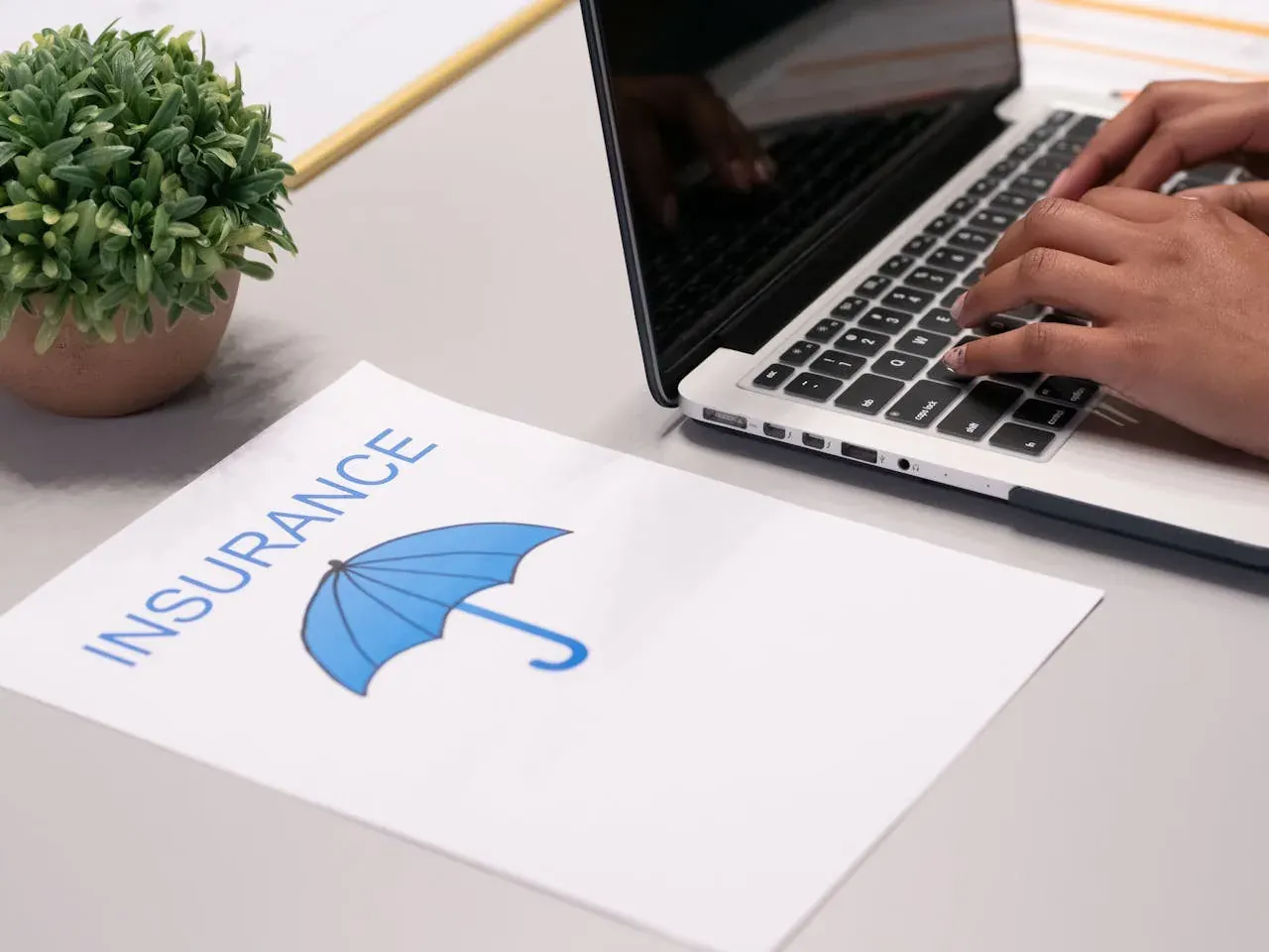 Hands typing on a laptop beside a printed sheet that reads Insurance.
