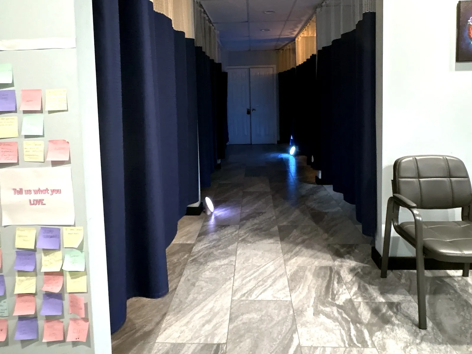 The treatment hallway in our Morristown office: each treatment space closed off by a navy privacy curtain, soft lights along the floor, and a wall of colorful patient sticky notes.