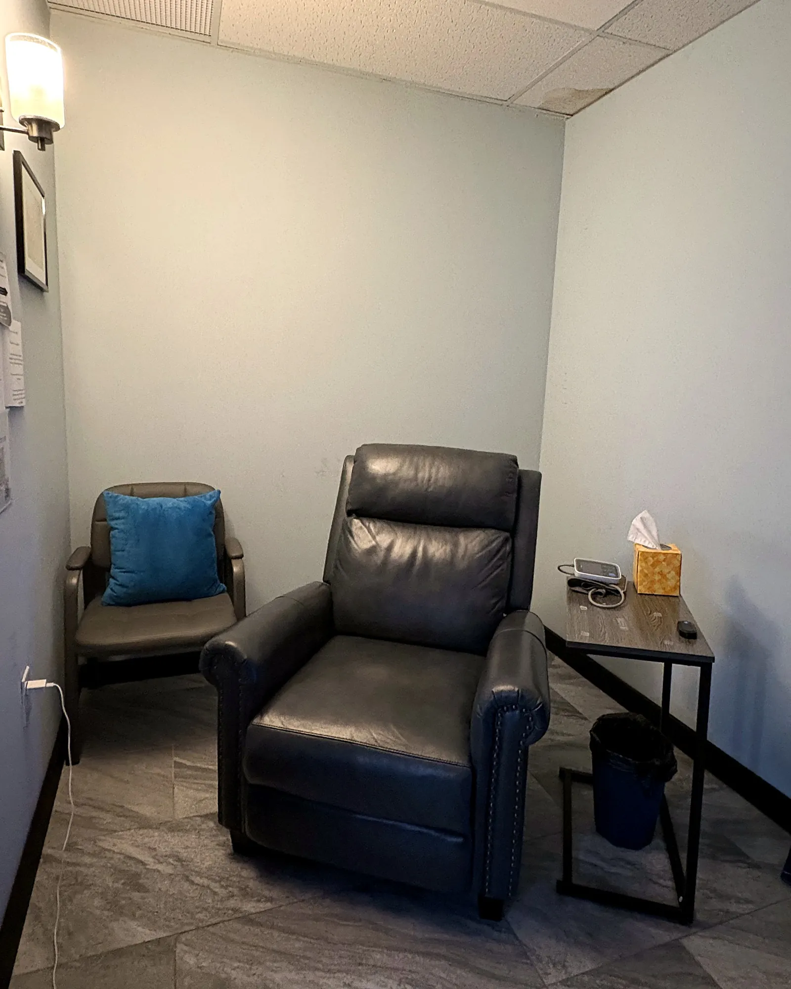 A private treatment space in our Morristown office: a gray leather recliner, a side chair with a blue pillow for anyone who comes with you, and a side table with tissues and a blood pressure monitor.
