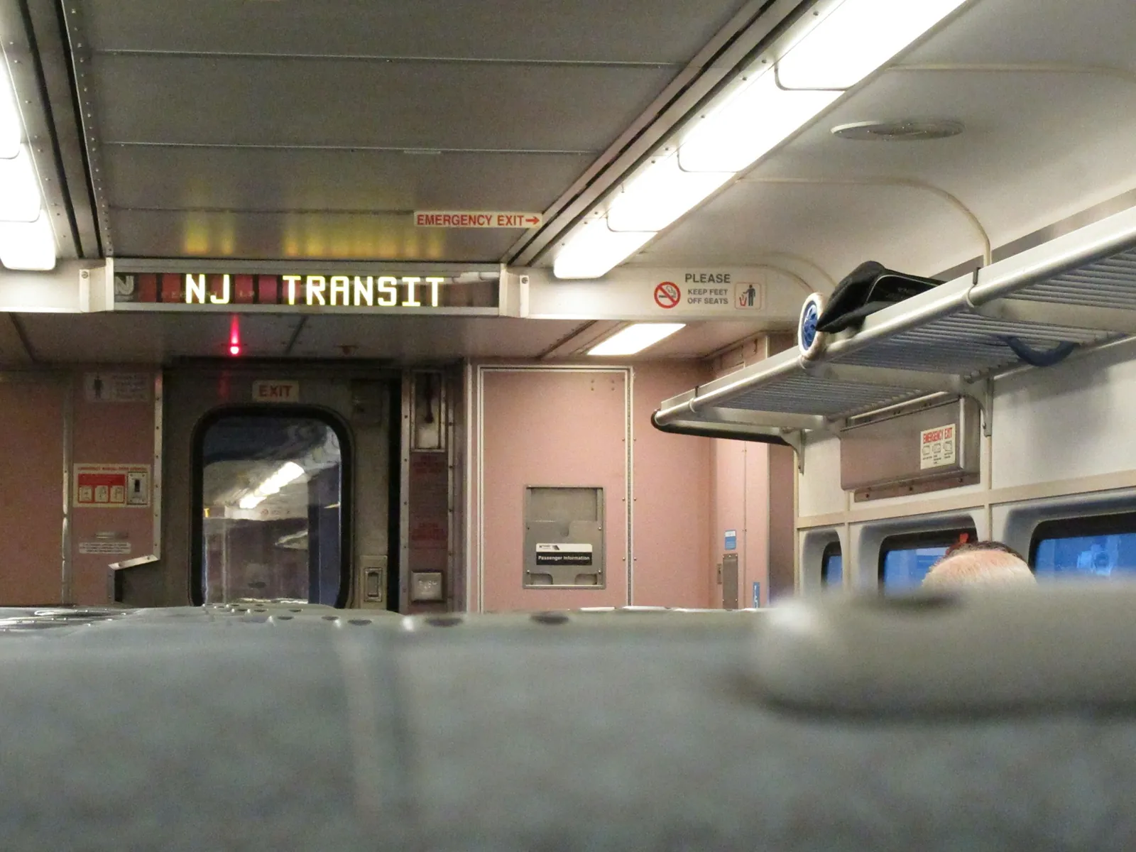 The inside of an NJ Transit train car, its destination sign lit above the door.
