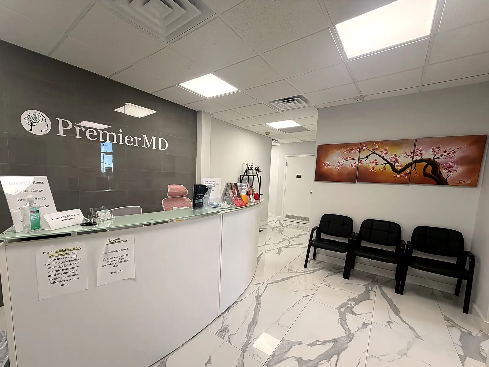 The Nutley reception: a curved white front desk below the PremierMD sign, marble floors, and waiting chairs beneath a cherry-blossom painting.