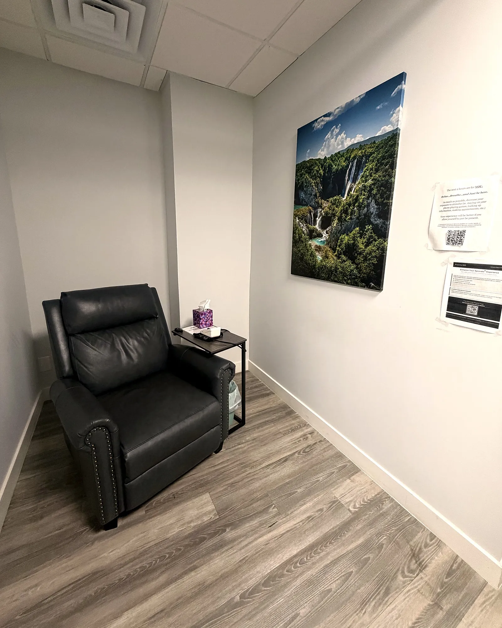 A private treatment room in our Nutley office: a black leather recliner and side table beside a large print of a forest waterfall.