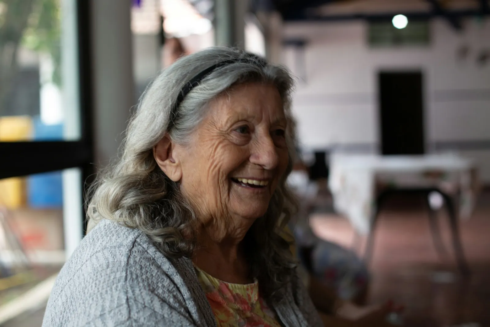 An older woman with gray hair laughing as she talks with someone off camera.