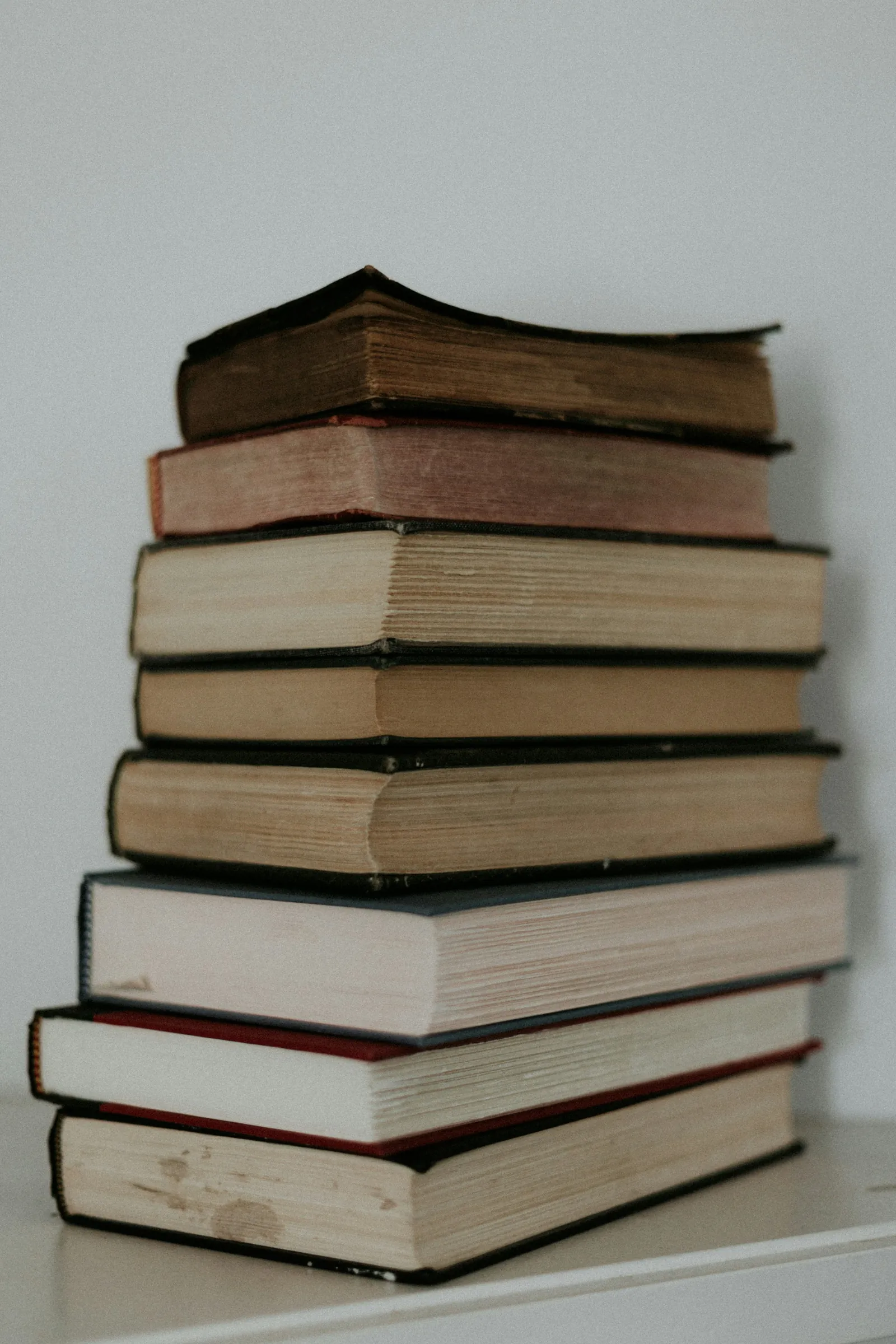 A tall stack of old hardback books on a white table.