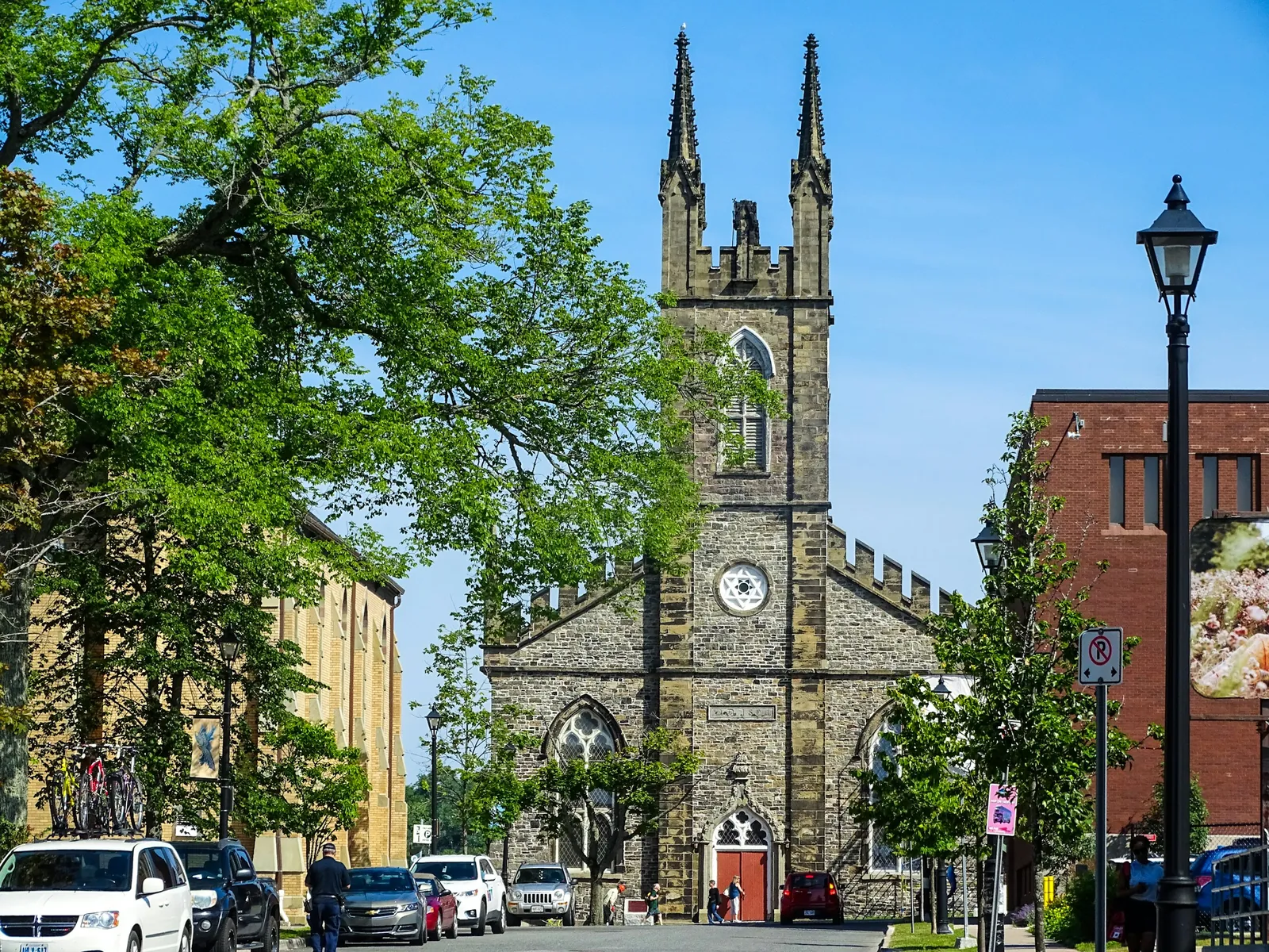A stone church tower with a clock above a tree-lined downtown street.
