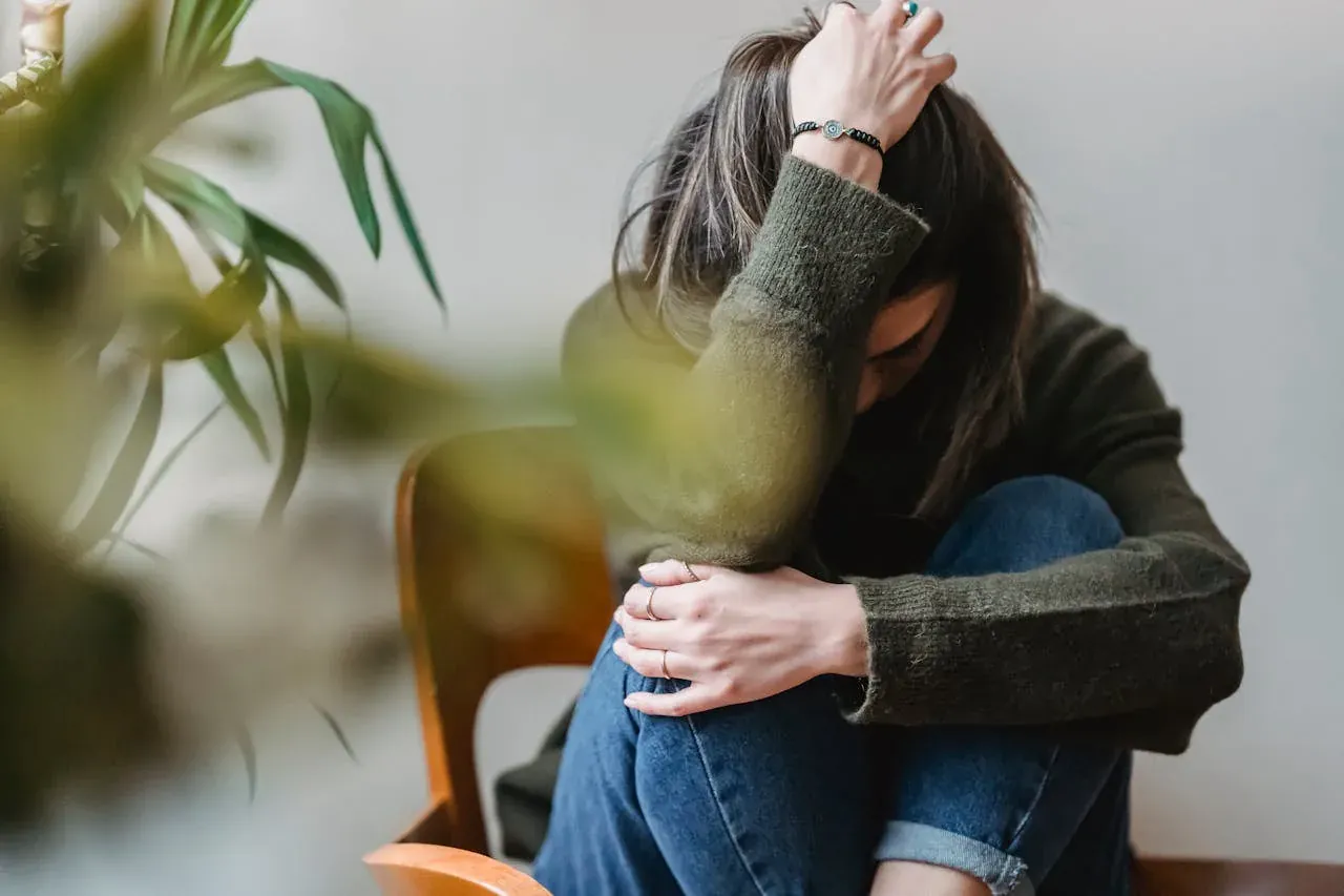 A woman curled up in a chair, her face hidden in her arm, crying.