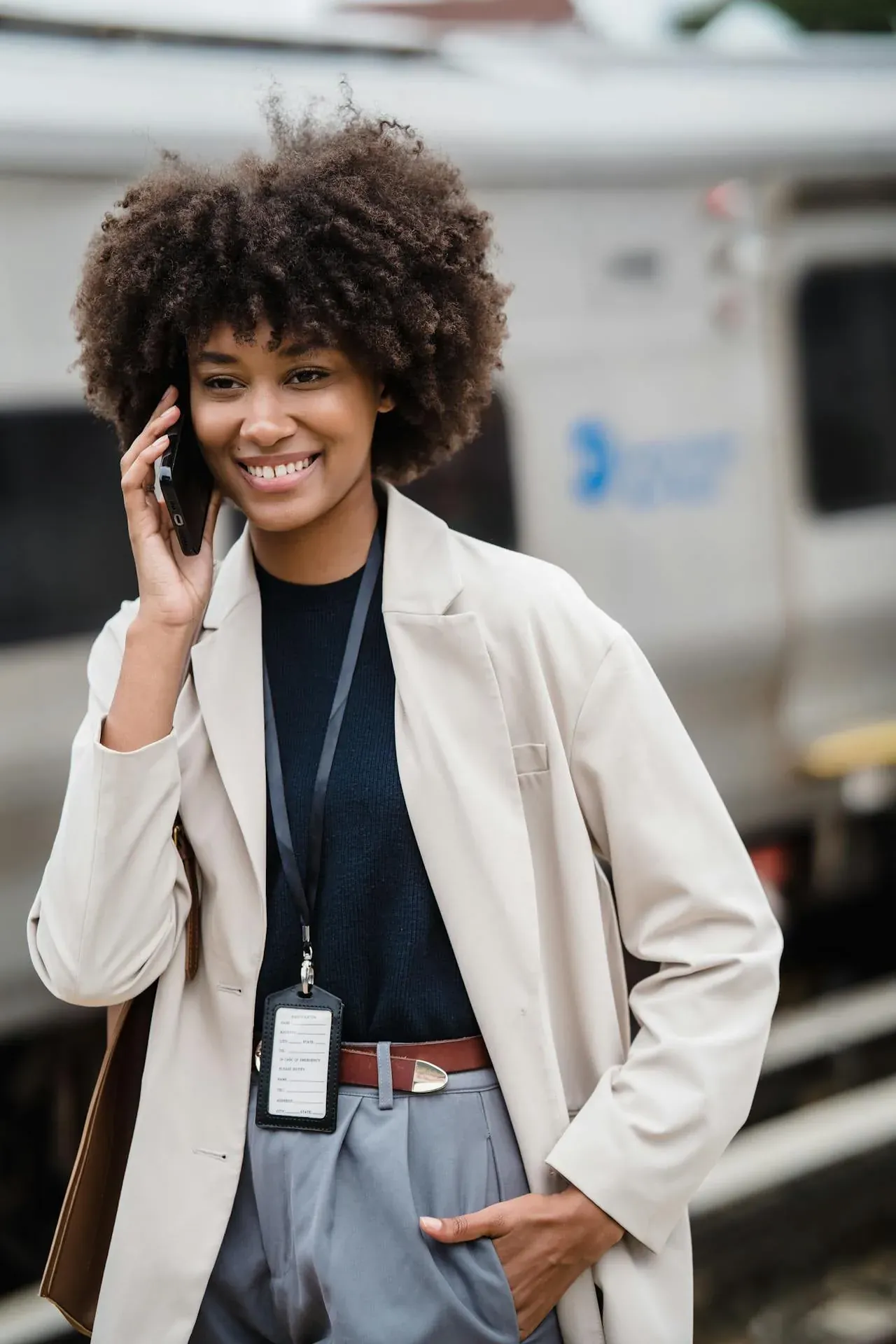 A smiling young woman with a curly afro talking on her phone as she walks outdoors.